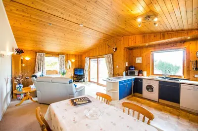 a kitchen and living room with a table in a room at Raven Lodge with beautiful views of Loch Dochart in Crianlarich