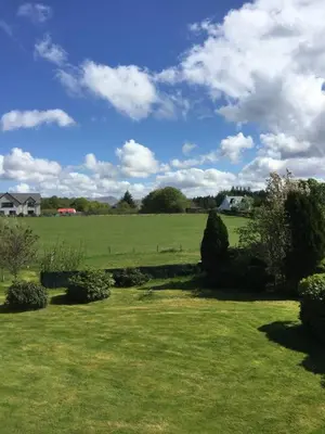 a green field with bushes and a sky with clouds at Coel Ila in Benderloch