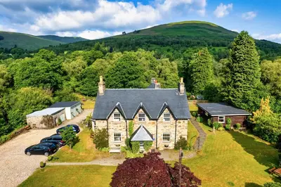 an old stone house with cars parked in front of it at Mansewood Country House in Lochearnhead