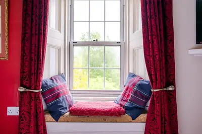 a window seat with red curtains and blue pillows at Mansewood Country House in Lochearnhead