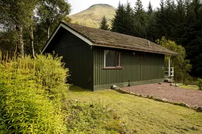 a green building with a mountain in the background at 2 bedroom lodge with free WiFi and mountain view in Crianlarich