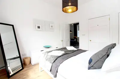 a white bedroom with a bed and a mirror at Stylish Flat in 1860's Listed Building in Edinburgh