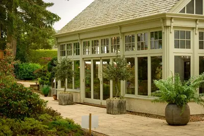 a large conservatory with windows and potted trees at Cairn Lodge in Auchterarder