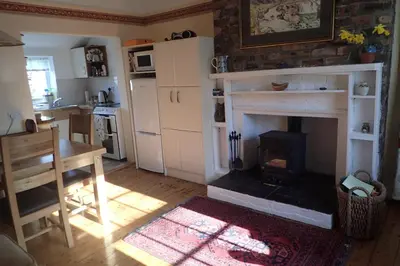 a living room with a fireplace and a table and a kitchen at Laich Cottage in Appin