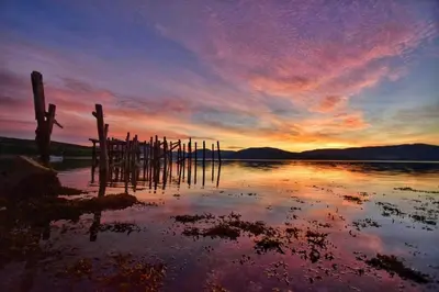 a sunset over a body of water with wooden posts at Old Fisherman's Cottage in Rothesay