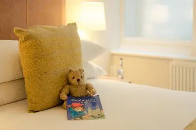 a teddy bear sitting next to a book on a bed at PREMIER SUITES PLUS Glasgow George Square in Glasgow