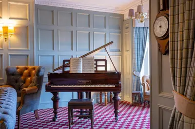 a piano in a living room with a clock at Knipoch House Hotel in Oban