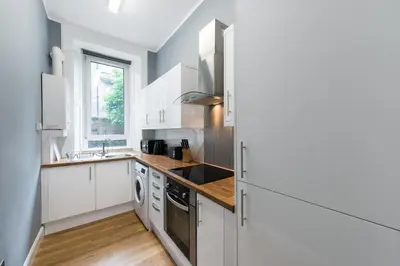 a kitchen with white cabinets and a wooden floor at City Centre, 5 star Ground Floor in Edinburgh