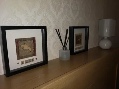 two framed pictures on a wooden shelf with a lamp at Sleep Well Apartment in Glasgow