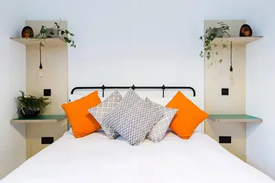a bedroom with a white bed with orange and grey pillows at The Plywood Flat, Modern Style In A Traditional Tenement in Edinburgh