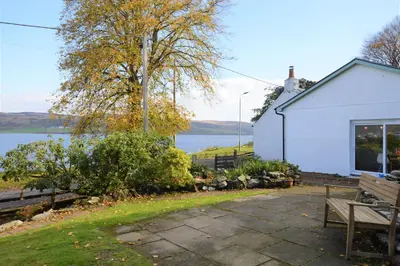a building with a bench next to a lake at Gate Cottage in Tighnabruaich