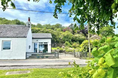 a white house with a gate and a fence at Gate Cottage in Tighnabruaich