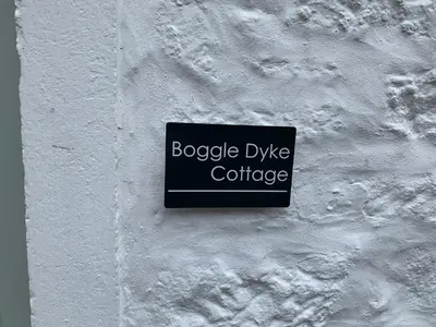 a sign on the side of a white wall at Boggle Dyke Cottage in Thornhill