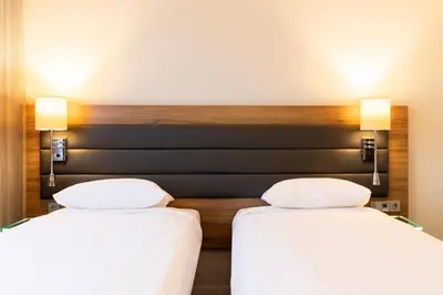 two beds in a hotel room with white sheets at Moxy Edinburgh Airport in Ingliston