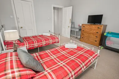 a bedroom with two beds and a tv and a dresser at Panoramic Sea Views - Stunning 3BD Apt & Balcony in Oban