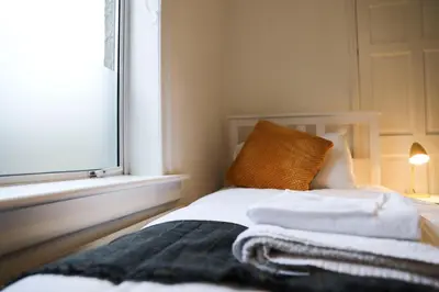 a bedroom with a bed with white sheets and a window at Baron View Apartment in Paisley