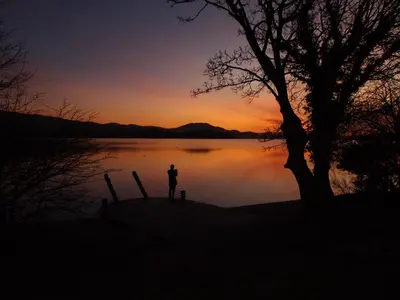 a person standing in front of a lake at sunset at The Lodge On Loch Lomond Hotel in Luss