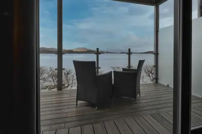 a balcony with two chairs and a view of the water at The Lodge On Loch Lomond Hotel in Luss