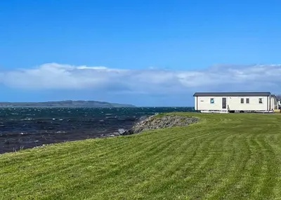 a house on a hill next to the ocean at Ryan Bay Holiday Park in Innermessan