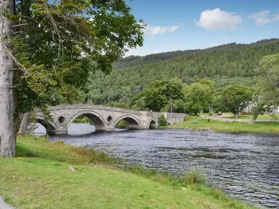a stone bridge over a river in a park at Ardchoille Cottage in Fortingall