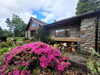 a stone house with pink flowers in front of it at Loch Lomond shore Boat House in Balmaha