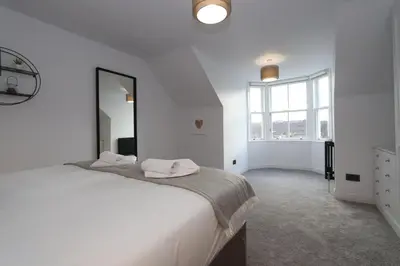 a white bedroom with a large bed and a large mirror at Dollar Apartments-41 Bridge Street in Dollar