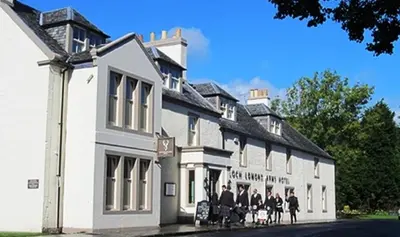 a group of people standing outside of a white building at The Loch Lomond Arms Hotel in Luss
