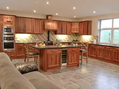 a kitchen with wooden cabinets and a large island at Liftingstane Farmhouse in Closeburn