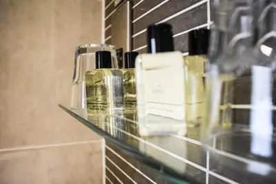 a glass shelf in a bathroom with bottles on it at Dalziel Park Hotel in Motherwell