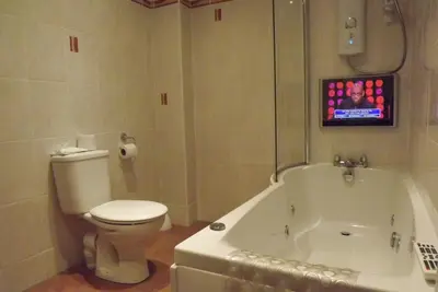 a bathroom with a toilet and a tub with a tv at Glazert Country House Hotel in Lennoxtown