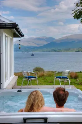 a man and a woman sitting in a hot tub overlooking a lake at Seabank House in Oban