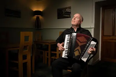 a man sitting in a chair playing an accordion at The Trout Fly Guest House in Port Ellen