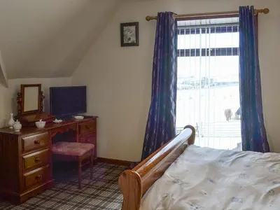 a bedroom with a bed and a dresser and a window at Old Stable Cottage in Uplawmoor