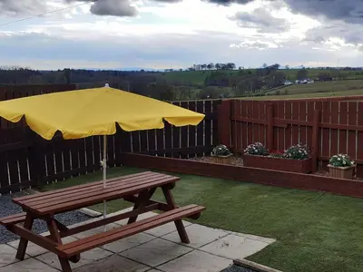 a wooden picnic table with a yellow umbrella at Old Stable Cottage in Uplawmoor