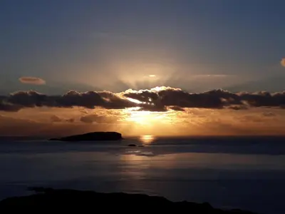 a sunset over the ocean with the sun hiding behind clouds at Garragh Mhor in Oban