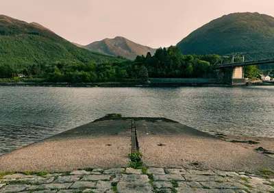 a bridge over a body of water with a mountain at Loch Leven Hotel & Distillery in Glencoe