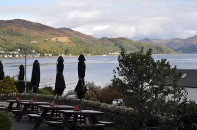 a group of tables with umbrellas next to a lake at Kames Hotel in Tighnabruaich
