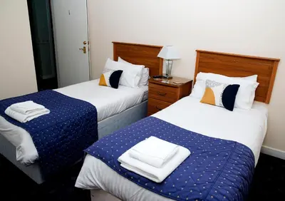 two beds in a hotel room with towels on them at Herdshill Guest House in Wishaw