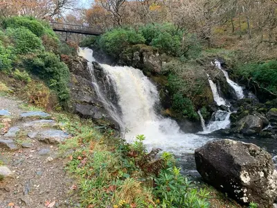 a waterfall on the side of a hill with a bridge at Ben Lomond Lodge in Rowardennan