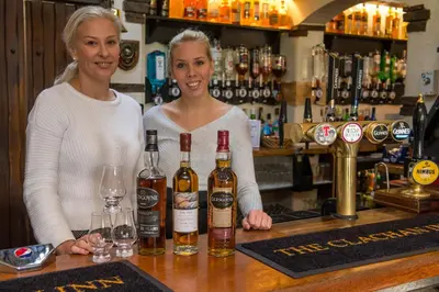 two women standing behind a bar with bottles of wine at The Clachan Inn in Drymen