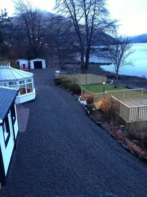 a house with a boat parked on a gravel driveway at Lochside Guest House in Arrochar