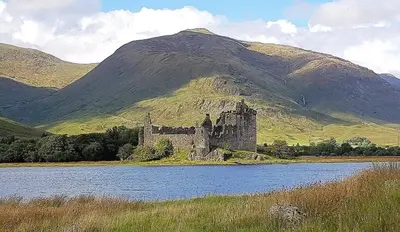 a castle in the middle of a lake in front of a mountain at The Nest Glamping Pod in Dalmally