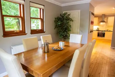 a dining room with a wooden table and white chairs at Bonnie Banks Cottage in Balloch