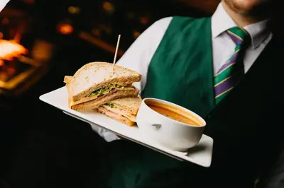 a man holding a plate with a sandwich and a cup of coffee at Ingliston Country Club Hotel in Bishopton