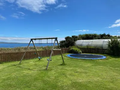a swing set in a grassy yard with the ocean at Portbahn, Bruichladdich in Bruichladdich