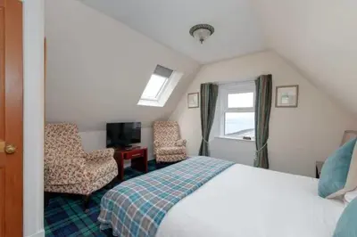a bedroom with a bed and two chairs and a television at Kilchrenan House in Oban