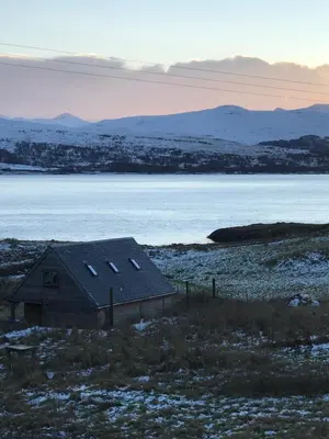a small house in a field with a body of water at Tigh a Chabar in Lochaline