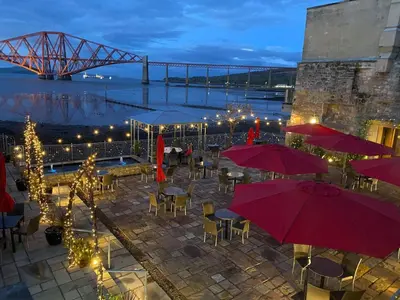 a patio with tables and umbrellas with a bridge in the background at Orocco Pier in Queensferry