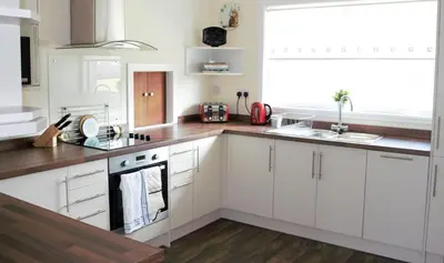 a kitchen with white cabinets and a sink and a window at The Glebe, Am Fasgadh in Bowmore