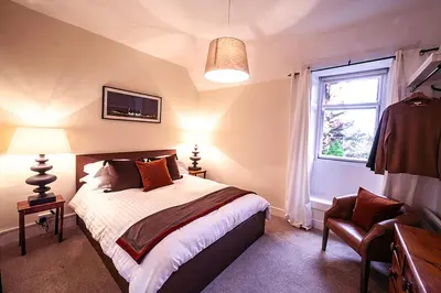 a bedroom with a bed and a window and a chair at Butler's Apartment. Flat 5, Dalmore House, Helensburgh, Scotland G84 8JP in Helensburgh